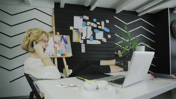 Businesswoman talking on phone and sitting with legs on table — Stock Photo, Image