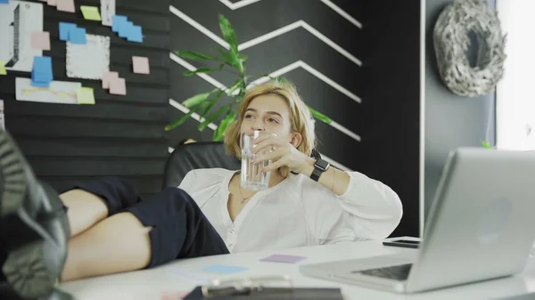 Happy business woman drinks water with Legs on the table — Stock Photo, Image