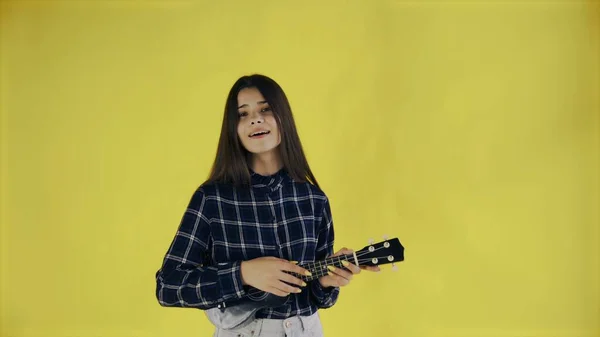 Young girl singing and playing ukulele on yellow Background in Studio — Stock Photo, Image