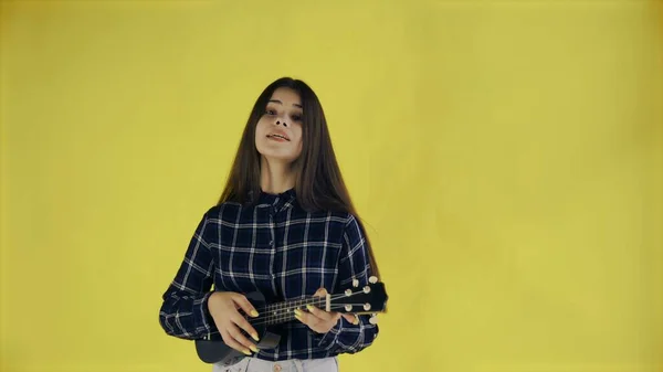 Tânără fată cântând și jucând ukulele pe fundal galben în Studio — Fotografie, imagine de stoc
