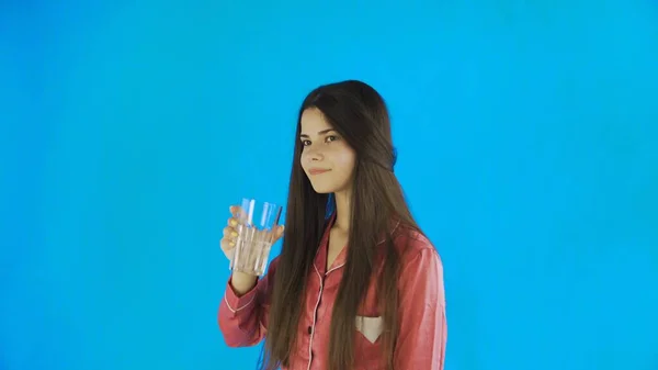 Ragazza caucasica adolescente che beve un bicchiere d'acqua. Giovane donna che beve acqua da vetro su sfondo blu in studio — Foto Stock