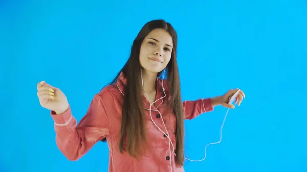 Mujer joven bailando mientras escucha música en auriculares sobre fondo azul —  Fotos de Stock