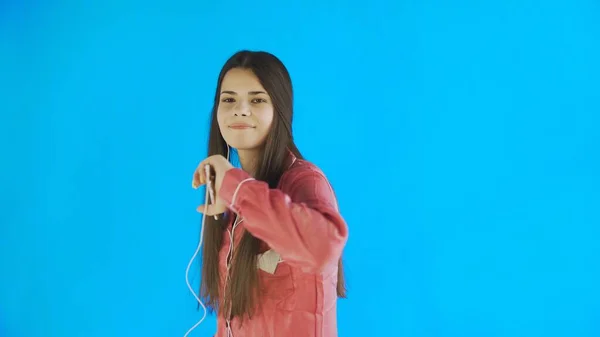 Young woman dancing while listening to music in headphones on blue background — Stock Photo, Image