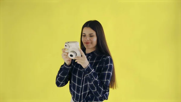 Portret van mooie Brunette gebruikt Retro Camera op gele achtergrond in Studio. Jonge vrouw neemt foto. — Stockfoto