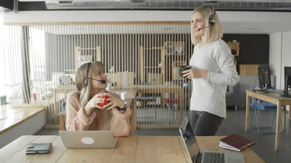 Female worker with headhones on head are drinking tea and chatting during lunch break at work — Stock Photo, Image