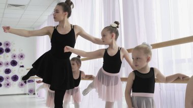 Öğretmenler küçük balerinlere nasıl dans edileceğini gösterirler. Bale okulundaki kız dansçı dans etmeyi öğreniyor. Eğitimde zıplayan genç balerinler. Bale okulu..