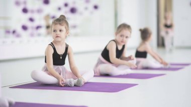 Dans okulunda esneme hareketleri yapan sevimli küçük balerinler. Sevimli küçük kız dans okulunda egzersiz yapıyor, bale çalışmadan önce esneme hareketleri yapıyor. Çocuklar, disiplin kavramı