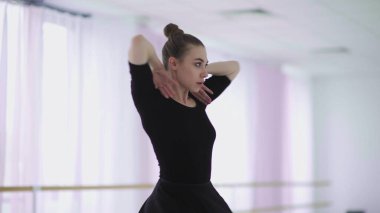 Siyah sırt çantalı profesyonel bir balerin büyük bir eğitim salonunda dans ediyor.