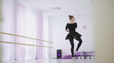 Siyah sırt çantalı profesyonel bir balerin büyük bir eğitim salonunda dans ediyor.