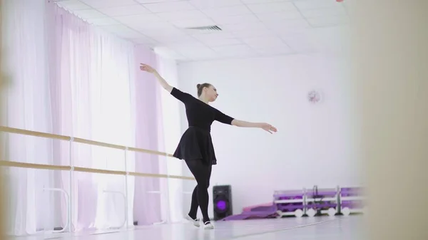 A professional ballerina in a black pack dances in a large training hall — Stock Photo, Image