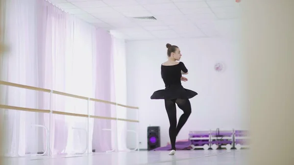 A professional ballerina in a black pack dances in a large training hall — Stock Photo, Image