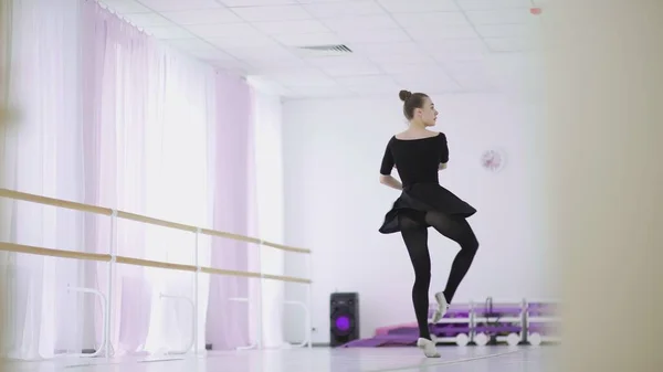A professional ballerina in a black pack dances in a large training hall Stock Image