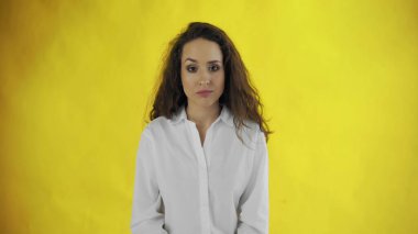 Kendine güvenen, uzun saçlı bir kadın sarı arka plandaki kameraya bakar.