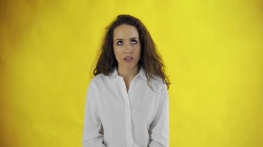 Kendine güvenen, uzun saçlı bir kadın sarı arka plandaki kameraya bakar.