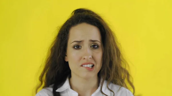 Jovem bela mulher morde lábio e fica em estúdio com fundo amarelo . — Fotografia de Stock