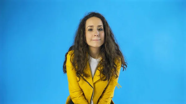 Happy Pretty Woman in gelber Jacke Augenzwinkern im Studio mit blauem Hintergrund. — Stockfoto