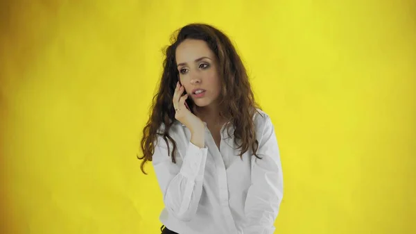 Mujer de negocios seria hablando de teléfono móvil sobre fondo amarillo. Retrato de una joven empresaria llamando al estudio. Profesional femenino tiene conversación móvil en el teléfono inteligente —  Fotos de Stock