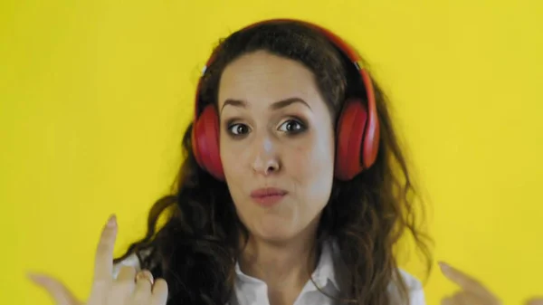 Mulher ouvindo música com fones de ouvido vermelhos no estúdio com fundo amarelo . — Fotografia de Stock