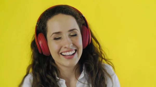 Woman listening to music with red headphones in Studio with yellow Background. — Stock Photo, Image