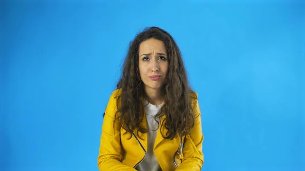 Enttäuschte und sehr traurige junge Frau weint fast im Studio mit blauem Hintergrund. — Stockfoto
