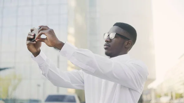 Серьезный афро-американский бизнесмен делает селфи на своем смартфоне возле своего офиса — стоковое фото