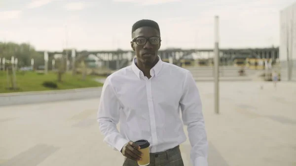オフィスに歩いている間に白いシャツとグレーのパンツを着たスタイリッシュなアフリカ系アメリカ人ビジネスマンがコーヒーを飲む — ストック写真