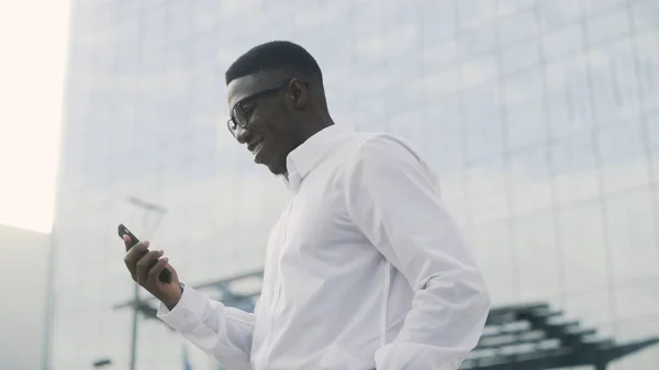 スマートフォンでオンライン成功を祝うアフリカ人男性,屋外 — ストック写真