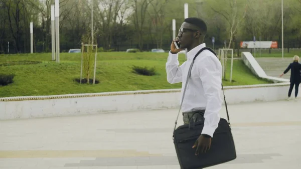 African American Businessman in glasses walking into office and talking on cell phone