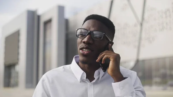 Joven empresario africano con aparatos ortopédicos hablando por teléfono celular en el parque de la ciudad — Foto de Stock