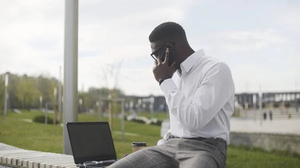 Empresario africano serio con gafas hablando por teléfono celular en el parque de la ciudad — Foto de Stock