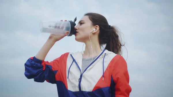 Esmer kız parkta koştuktan sonra soğuk su içiyor..