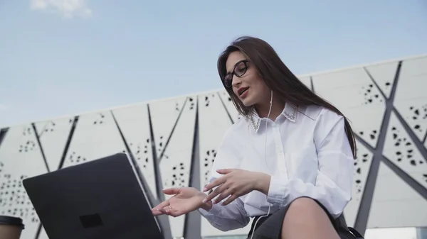 Young caucasian business woman with long hair talk on skype using laptop sitting outdoor. — Stock Photo, Image