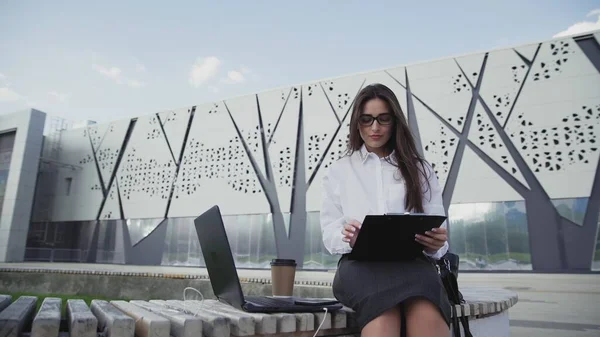 Pretty businesswoman talking on cellphone and comparing data on laptop and documents — Stock Photo, Image