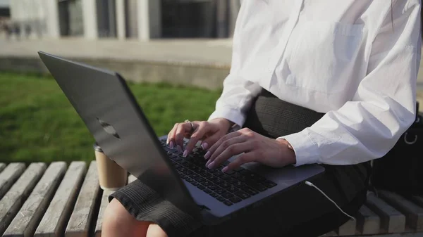 Young business woman sitting outdoors on bench with laptop and working. Stock Image