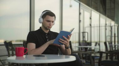 Kulaklıkla müzik dinleyen ve kitap okuyan yakışıklı adam.