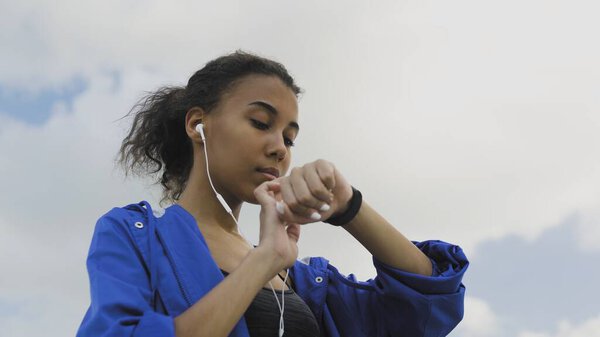 Афро-американская бегунья в наушниках с помощью фитнес-браслета перед пробежкой
