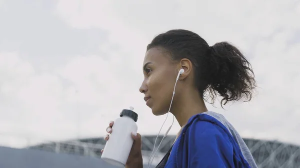 Afro-american runner woman Drinking Water or isotonic After Running. Portrait Fitness Woman Drinking Water From Bottle.