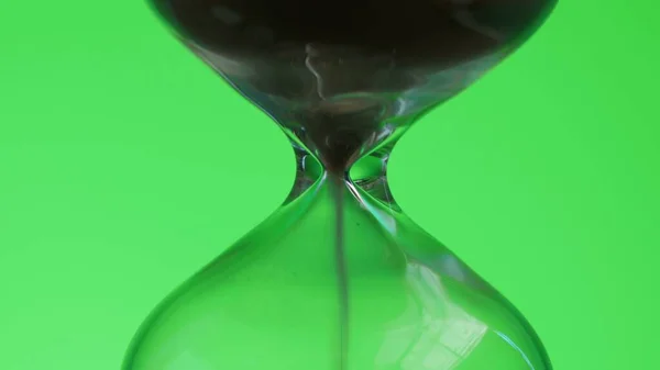 Hourglass on green background. Sand is pouring from one part to another. Time and transience concept.