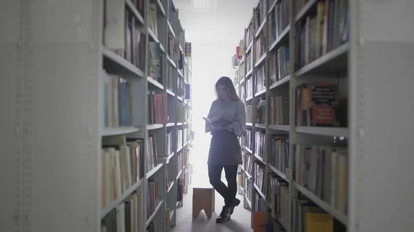 Young student girl taking book from shelf in university library. — Stock Photo, Image