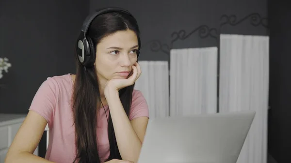 Красива жінка в навушниках слухає музику з ноутбука, сидячи в спальні — стокове фото