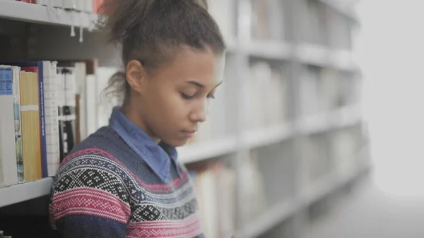 Mujer afroamericana joven está leyendo libro sentado en el suelo en la biblioteca universitaria . —  Fotos de Stock