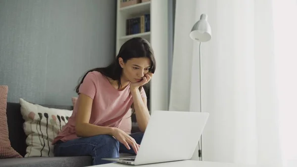 Нудна жінка працює з ноутбуком зручно сидить вдома — стокове фото
