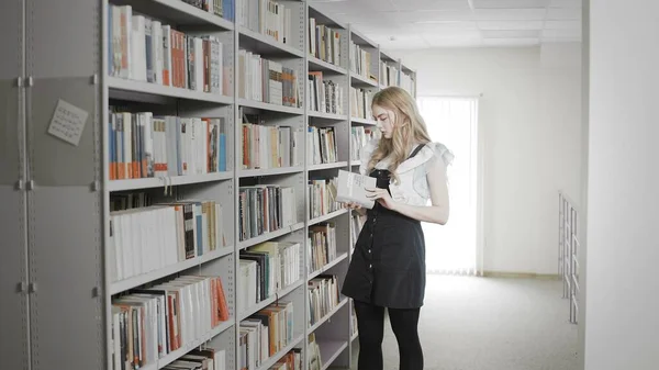 Rubia estudiante tomando libro de la estantería en la biblioteca universitaria . — Foto de Stock