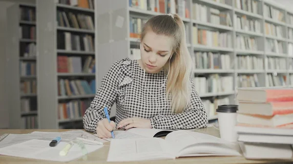 Jovem estudante escrevendo em seus livros didáticos na biblioteca — Fotografia de Stock