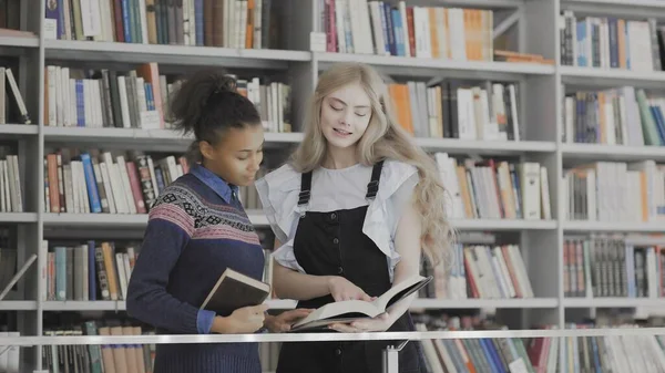 Mujeres europeas y afroamericanas están leyendo libro en biblioteca — Foto de Stock