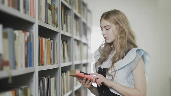 Jovem loira estudante mulher tomando livro de prateleira na biblioteca da universidade . — Fotografia de Stock