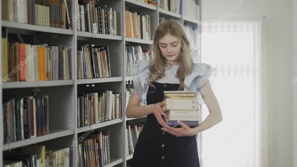 Beautiful young blonde student woman walking in university library with many books in hands