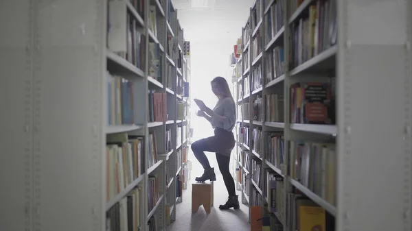 대학 도서관에서 책꽂이에서 책을 꺼내는 젊은 여학생. — 스톡 사진