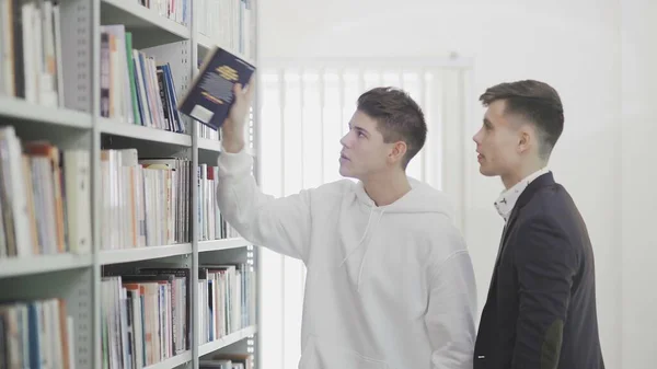 Два студента ищут книгу на книжных полках в библиотеке в колледже — стоковое фото