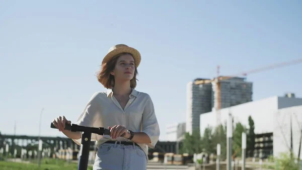 Mujer joven en sombrero de paja caminando con ella la patada eléctrica scooter — Foto de Stock